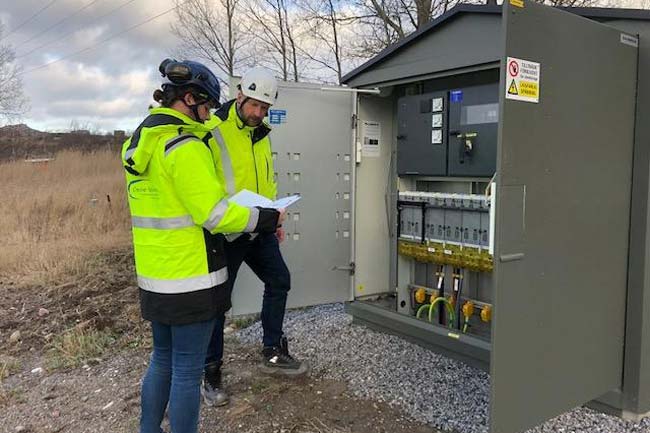 Två kollegor står vid ett elskåp